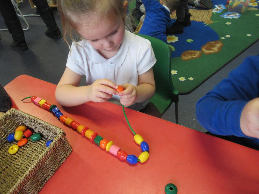Lottie using her fine motor skills to thread beads