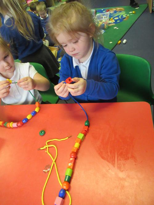 Megan is practicing threading beads during a fine motor activity